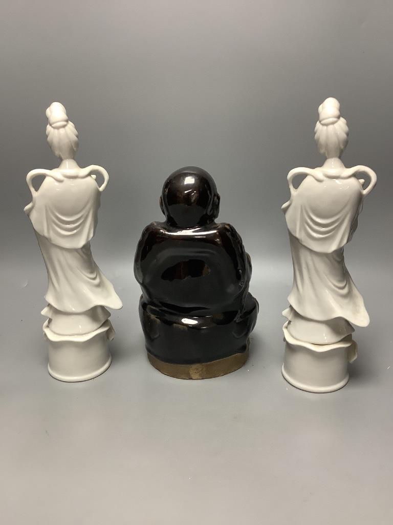 A Chinese dark brown glazed Buddha, and a pair of blanc de chine figures of Guanyin, tallest 30cm